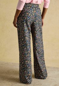 Kvetinové nohavice s širokými nohavicami na tmavomodrom pozadí, s jasným vzorom malých viacfarebných kvetov. Viditeľný elastický pás.