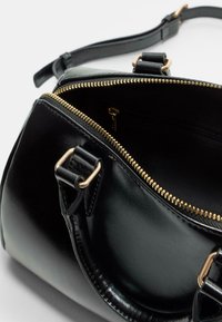 Sac à main en cuir noir à la forme arrondie, fermeture zippée et quincaillerie dorée. Il possède une texture lisse et une poche intérieure plaquée.