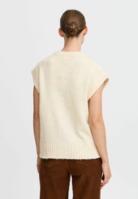 Beige, �ärmelloser Strickpullover mit geripptem Saum, weicher Textur und lockerer Passform, kombiniert mit braunen Cordhosen.