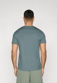 T-shirt da uomo a maniche corte in tessuto teal softo con scollatura rotonda e un piccolo dettaglio sulla parte posteriore, abbinato a pantaloni corti verde chiaro.