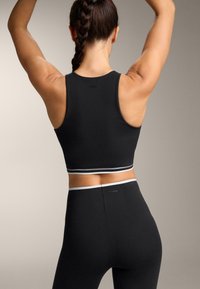 Zwarte atletische cropped top met een ronde halslijn en brede bandjes, voorzien van witte accentstrepen aan de zoom, gecombineerd met bijpassende high-waisted legging.