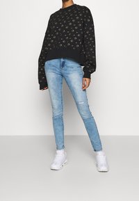 Sweatshirt noir court avec motif de cercles dorés sur toute la surface, associé à un jean skinny bleu clair et des baskets de sport blanches.