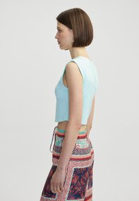 Top corto azzurro chiaro senza maniche. Abbinato a pantaloni multicolori patterned con accenti floreali e geometrici.