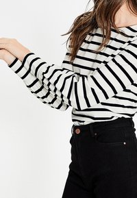 Schwarz-weißer gestreifter Langarmoberteil mit rundem Halsausschnitt und leicht puffigen Ärmeln, kombiniert mit hochgeschnittenen schwarzen Jeans.