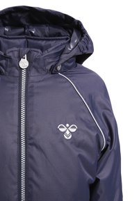 Granatowa kurtka z kapturem, z zamkiem z przodu, srebrne wykończenie na ramieniu i haftowane logo pszczoły na klatce piersiowej.