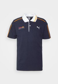 Polo-shirt marine avec un col blanc, des accents orange et le logo Red Bull Racing sur la poitrine. Fabriqué en coton, il présente une coupe classique et des manches courtes.