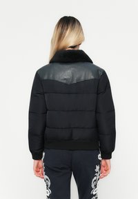 Svart dunjakke med en strukturert svart skinn yoke og svart faux pelshals. Har ribbestrikkede mansjetter og kant, med quiltet søm.