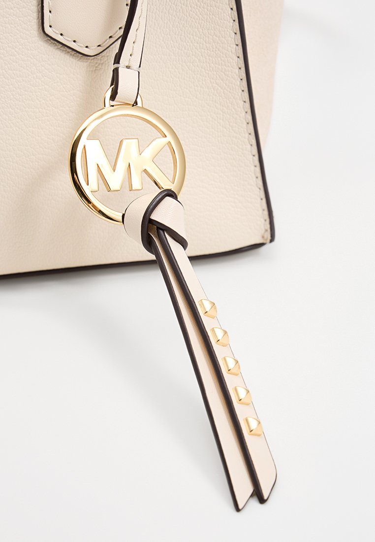 Beiger Handtaschen-Schlüsselanhänger mit goldenem, kreisförmigem Logo, strukturiertem Rand und Lederband mit goldenen Pyramidennieten.