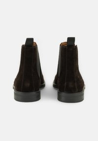 Bottines en suède marron avec une finition lisse, des panneaux élastiques sur les côtés et des languettes pour un enfilage facile ; semelles en caoutchouc plates avec un léger motif.