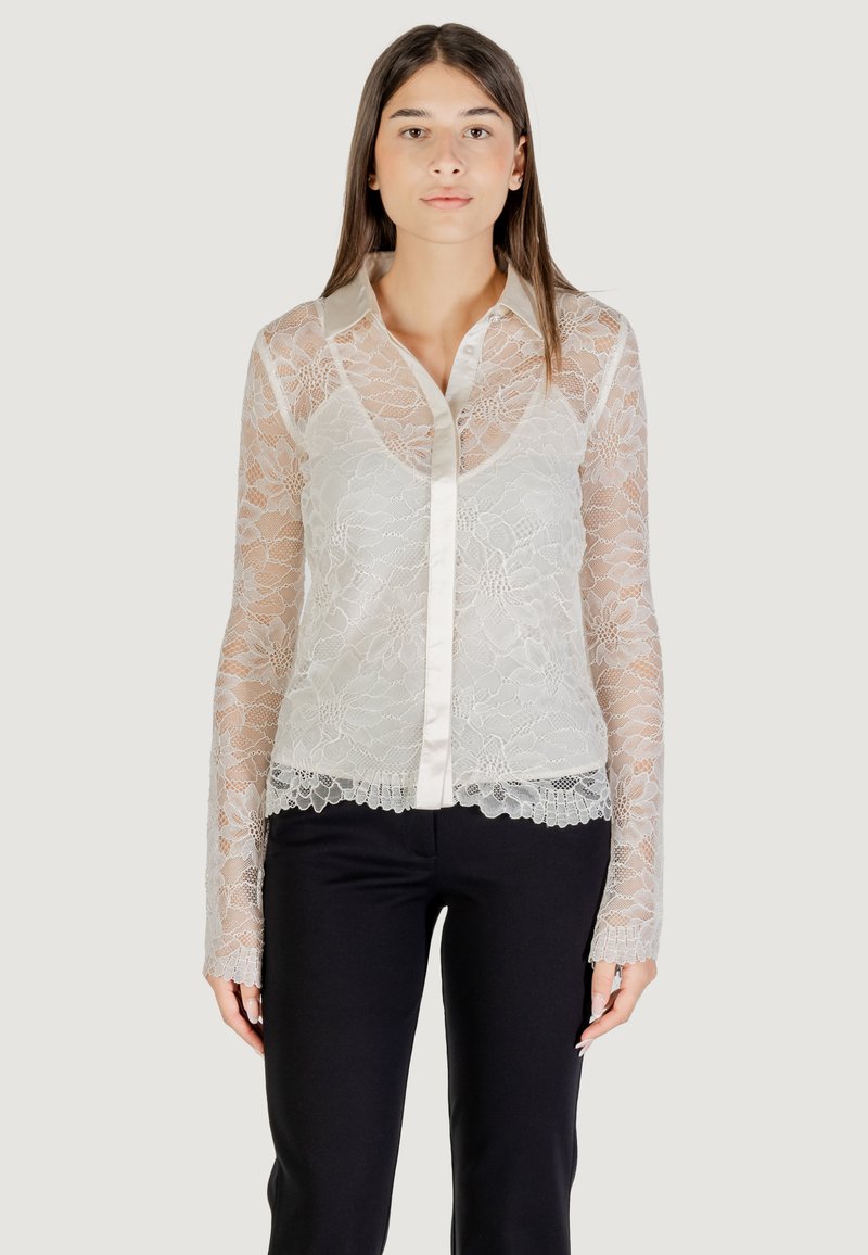 Blusa de encaje con mangas largas, color crema claro, cierre frontal con botones, cuello de satén y patrones florales en el dobladillo y las mangas.