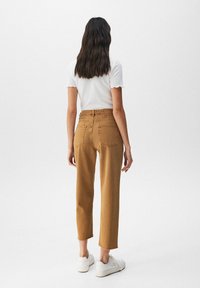 Pantalon taille haute couleur miel à jambe droite, avec poches, ourlet effiloché, associé à des baskets blanches et un haut blanc ajusté.