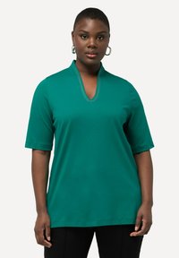 Top corto de color verde azulado con escote en forma de V que presenta un detalle de costura decorativa. Tela suave y lisa con un corte relajado.