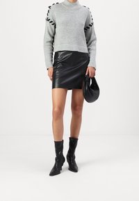 Pull gris tricoté avec des détails noirs, associé à une mini-jupe en cuir noire. Le modèle porte des bottines noires et tient un sac noir.