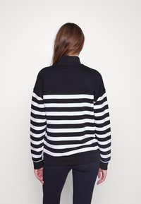 Sudadera a rayas en blanco y negro con un alto cuello y mangas largas, con puños y dobladillo acanalados para un ajuste relajado.