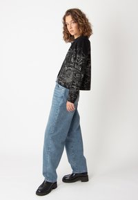 Svart kofta med ett strukturerat mönster i vitt, tillsammans med ljusblå vida jeans. Skorna är svarta plattformsskor.