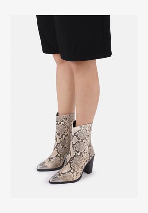 Beżowe botki z wężowej skóry za kostkę z ostrym noskiem i metalicznymi srebrnymi akcentami. Posiadają masywny obcas i zamek błyskawiczny z boku.