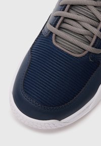 Chaussure de sport marine avec une tige en tissu texturé à rayures horizontales, accents en cuir lisse et lacets gris. Semelle en caoutchouc blanche.