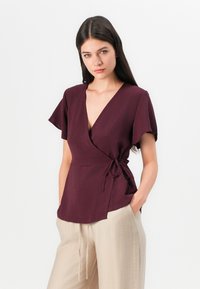 Burgundy wrap top with short, flutter sleeves; features a tie at the waist and a deep v-neck; made from a textured, lightweight fabric.