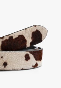 Cinturón de piel de vaca con una superficie texturizada que presenta manchas marrones y crema. Los extremos son puntiagudos y está parcialmente enrollado para dar perspectiva.