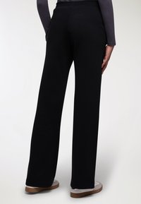 Czarne, szerokie spodnie wykonane z miękkiego materiału, z elastycznym paskiem w talii. Gładka faktura, pełna długość, zestawione z lekkim obuwiem.