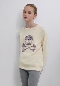 Sweat-shirt beige avec un motif coloré de crâne et os croisés, comprenant des motifs géométriques. Col rond et manches raglan.