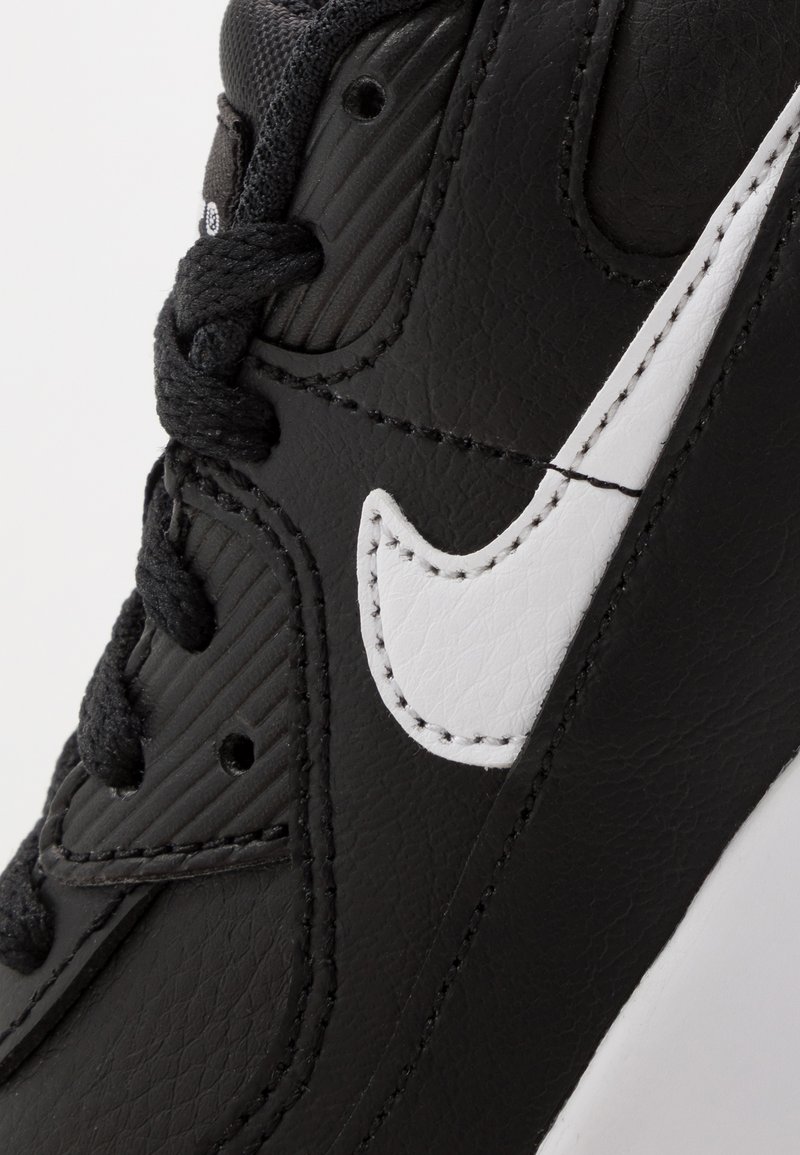Schwarze Sneaker aus strukturiertem Leder, mit einem weißen Nike-Swoosh-Logo, schwarzen Schnürsenkeln und einer Gummisohle mit sichtbaren Nähdetails.