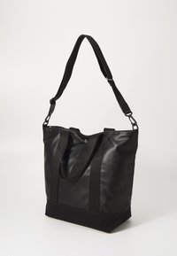 Sac fourre-tout en cuir noir avec des anses en tissu, présentant une forme structurée, une texture lisse et un panneau inférieur noir contrastant.