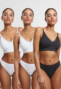Ensemble soutien-gorge et culotte en blanc, noir et gris. Le tissu présente une texture douce avec une bordure en dentelle le long du décolleté en V, mettant en avant un design simple.