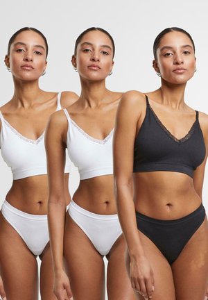 Completo reggiseno e slip bianco, nero e grigio. Il tessuto presenta una consistenza morbida con pizzo lungo lo scollo a V, evidenziando un design semplice.