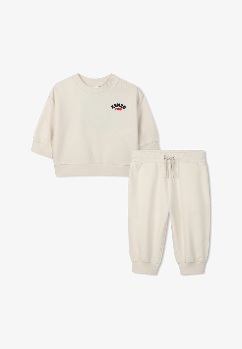 Felpa color crema con maniche corte e chiusura a bottoni, con la scritta "KENZO PARIS" ricamata. Pantaloni jogger abbinati con vita elastica.