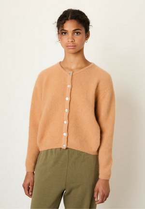 Gilet en tricot duveteux orange clair avec un col rond, des manches longues et six boutons sur le devant ; associé à un pantalon vert olive.