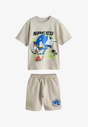 Bézs színű kisgyermek ruházat Sonic the Hedgehog grafikás pólóval, amely Sonic mozgását ábrázolja, valamint hozzáillő rövidnadrág Sonic emblémával és felirattal.