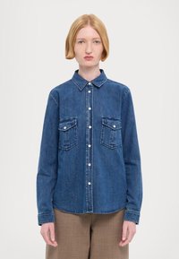 Τζιν πουκάμισο σε σκούρο μπλε, με μακριά μανίκια, κολάρο με κουμπιά, δύο τσέπες στο στήθος και μπροστινή κλείσιμο με κουμπιά. Λείος υφή, κλασικός σχεδιασμός.