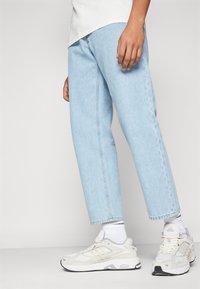 Jeans de mezclilla azul claro con corte recto, costuras cosidas y un acabado limpio, combinados con zapatillas deportivas blancas y calcetines blancos.