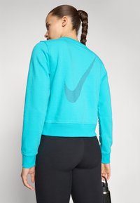 Türkisfarbenes Sweatshirt mit cropped Design, ausgestattet mit einem großen grauen Nike-Swoosh-Logo auf der Rückseite. Weicher Stoff, gerippte Bündchen und Saum.