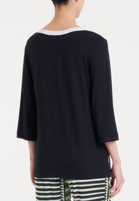 Maglietta nera a maniche lunghe con scollatura bianca, caratterizzata da una vestibilità comoda e una texture liscia e morbida. Il modello indossa pantaloni a righe.