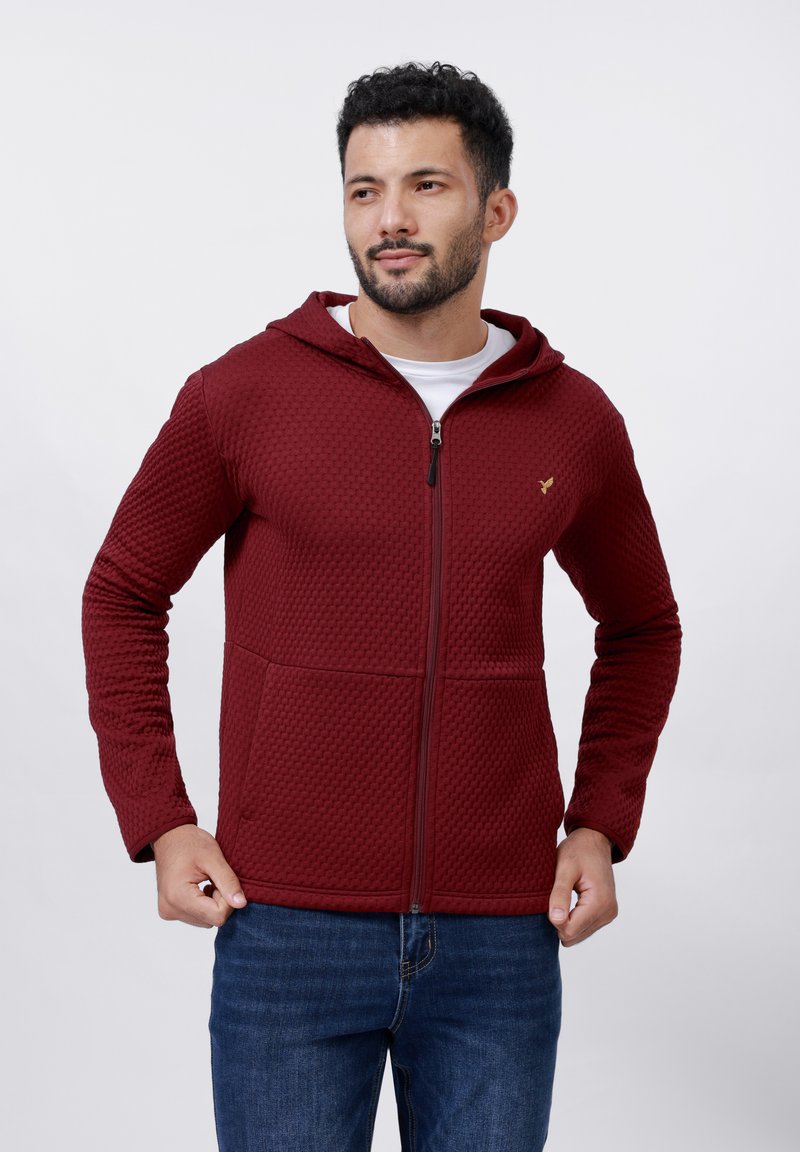 Bordo zip-up dukserica s teksturiranim uzorkom, prednjim džepovima i kapuljačom s vezicom. Dizajnirana je s ravnim krojem i rebrastim rukavima.