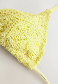 Geel gehaakte bralette met een bloemenpatroon, textuurstof en verstelbare bandjes. Bevat een klein gouden hardwaredetail.