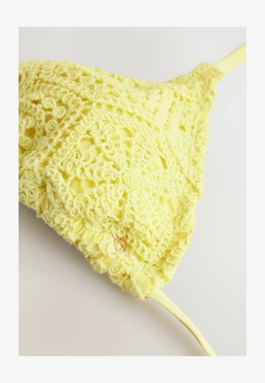 Gelbes gehäkeltes Bralette mit floralem Muster, strukturiertem Stoff und verstellbaren Trägern. Besitzt ein kleines Detail aus goldfarbenem Metall.