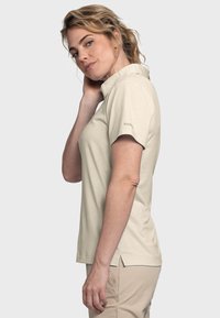 Beige Poloshirt mit kurzen Ärmeln, weichem Stoff und seitlichen Schlitzen. Leichtes Design mit genähten Akzenten am Kragen und Saum.