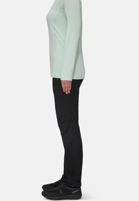 Mintgrön långärmad topp, svarta byxor med knäpaneler och svarta träningsskor. Slät tygtextur med en figurnära design.