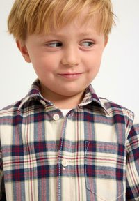 Koszula zapinana na guziki w czerwono-niebiesko-zieloną kratę na kremowym tle, z kołnierzykiem i kieszenią na piersi, wykonana z miękkiego materiału.