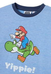 Blauwe katoenen t-shirt met een grafisch ontwerp van een karakter dat op een ander rijdt, met de tekst "Yippie!" in het wit eronder. Marineblauwe kraag accentueert het ontwerp.