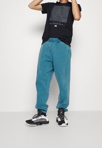 Černé tričko s grafickým designem, spárované s volnými, světle modrými tepláky. Černé a bílé tenisky s červenými akcenty.