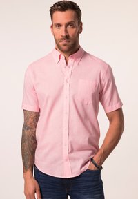 Camisa de botones de manga corta en tejido rosa claro, con cuello, bolsillo en el pecho y un corte relajado. Textura suave, diseño informal.