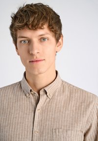 Camicia button-up marrone chiaro con righe verticali bianche, dotata di colletto e taschino sul petto. Tessuto liscio, dettagli minimi.