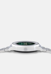 Hvid smartwatch med en rund urskive, grøn skive der viser tal, og en struktureret rem. Har en knap på siden til funktionalitet.