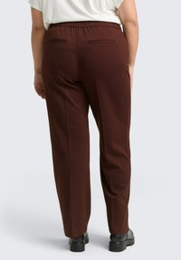 Pantalons marron ajustés avec une taille élastique, dotés de deux poches arrière et d'une coupe droite. Fabriqués dans un tissu doux au toucher lisse.