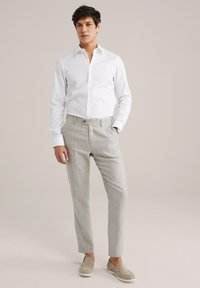 Bílá košile s dlouhým rukávem a límečkem, doplněná světlými šedými kalhotami s proužky. Ozdobeno knoflíkem v pase a světle hnědými slip-on botami.