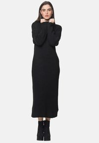 Schwarzes, geripptes Strickkleid mit hohem Kragen, langen Ärmeln und gerader Silhouette, das eine Länge bis zur Wade hat und aus strukturierter Stoff gefertigt ist.